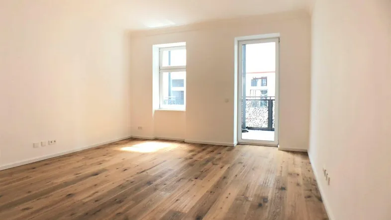 Helles Zimmer mit Holzboden und Zugang zu einem kleinen Balkon, ideal als Wohn- oder Schlafbereich.