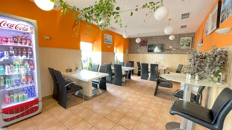 Geräumiger Restaurantbereich mit orangefarbenen Wänden, gefliestem Boden und mehreren Tischen und Stühlen für Gäste.