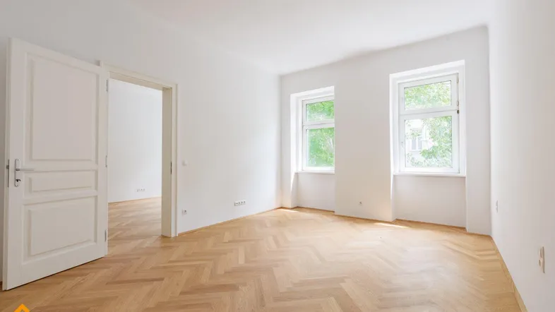Helles Zimmer mit Fischgrätparkettboden, weißen Wänden und Blick ins Grüne.