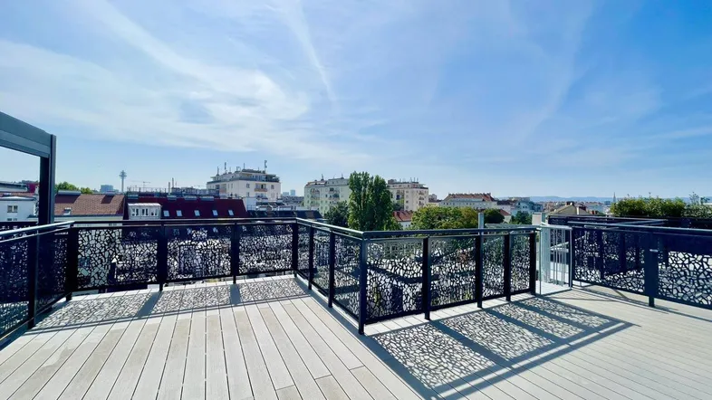 Geräumige Dachterrasse mit modernem Geländer und weitem Stadtblick unter blauem Himmel.