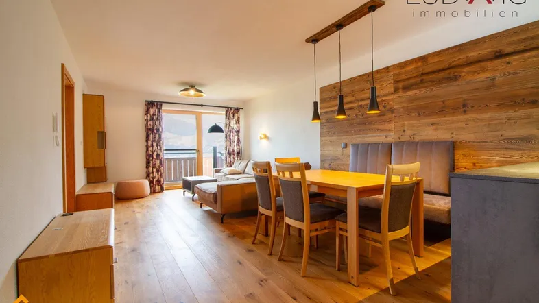 Geräumiger Wohn-Essbereich mit Holzboden, gemütlicher Sitzecke und Zugang zum Balkon.
