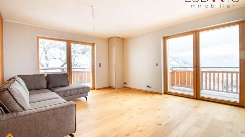 Helles Wohnzimmer mit modernem Sofa, Holzboden und Zugang zu einem Balkon mit Bergblick.