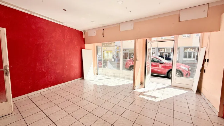 Geräumiger Ladenbereich mit großen Schaufenstern zur Straße, roter Akzentwand und hellen Fliesen.