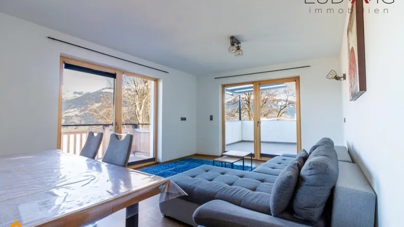 Geräumiger Wohn-Essbereich mit gemütlichem Sofa, Esstisch und Zugang zu einem Balkon mit Bergblick.