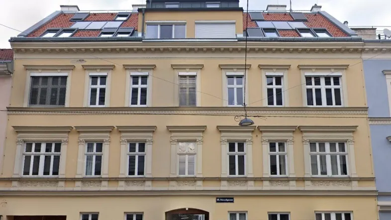 Mehrstöckiges Gebäude mit klassischer Fassade, vielen Fenstern und Solarpaneelen auf dem Dach.