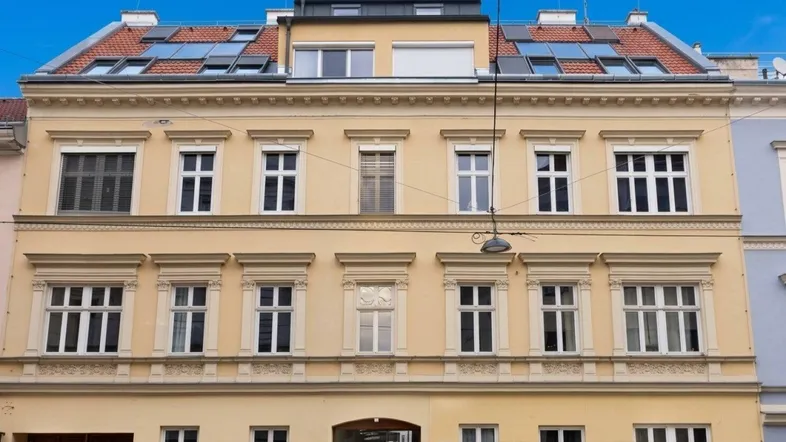 Die Fassade des Mehrfamilienhauses zeigt klassische Architektur mit modernen Dachfenstern und einer hellgelben Farbgebung.