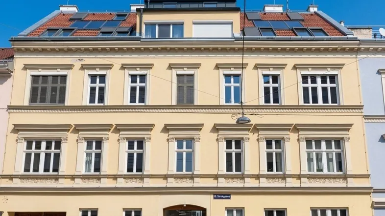 Historisches Gebäude mit gelber Fassade, vielen Fenstern und modernisiertem Dachbereich.