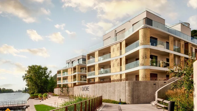 Moderne Wohnanlage am Seeufer mit Terrassen und Blick auf das Wasser unter bewölktem Himmel.