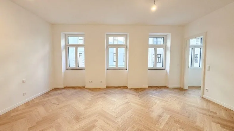 Helles Zimmer mit Fischgrätparkett und drei Fenstern, ideal als Wohn- oder Schlafzimmer.