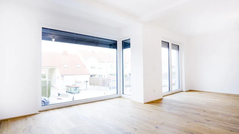 Heller, leerer Raum mit großen, modernen Fenstern und Holzboden, bietet viel Tageslicht und Blick ins Grüne.