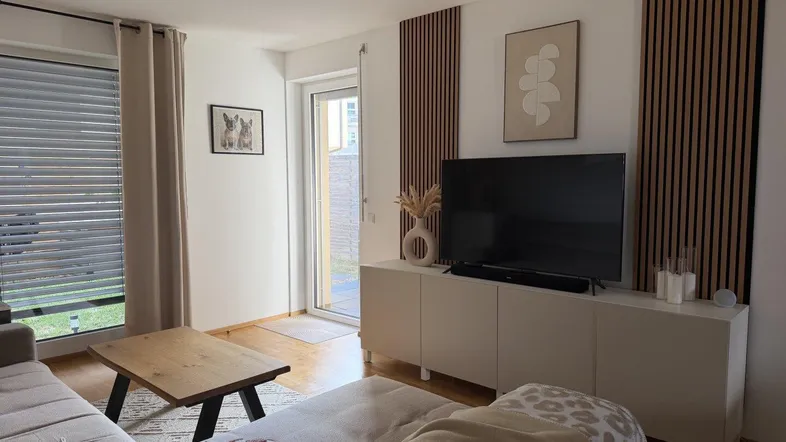 Helles Wohnzimmer mit beigem Sofa, Holztisch und modernem TV-Möbel, mit Zugang zum Außenbereich.