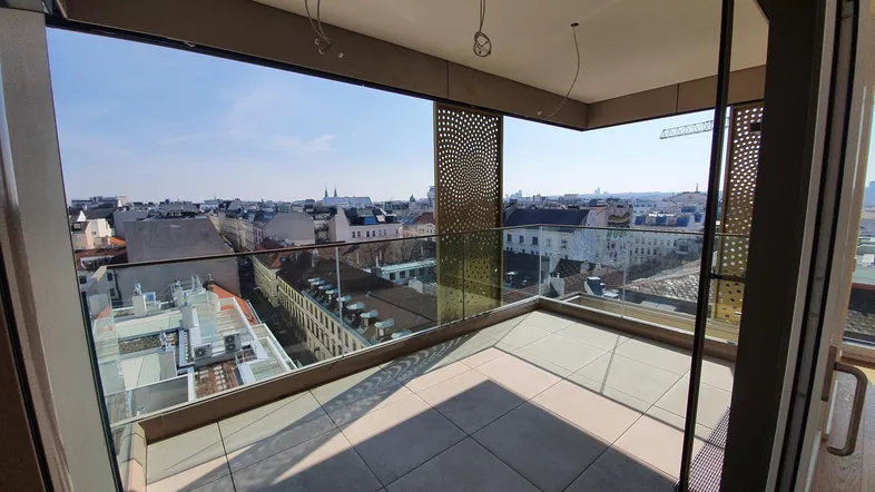 Geräumiger Balkon mit Glasgeländer und weitem Blick über die Stadt an einem sonnigen Tag.