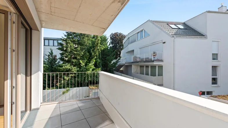 Geräumiger Balkon mit Fliesenboden und Blick auf die umliegenden Gebäude und Bäume.
