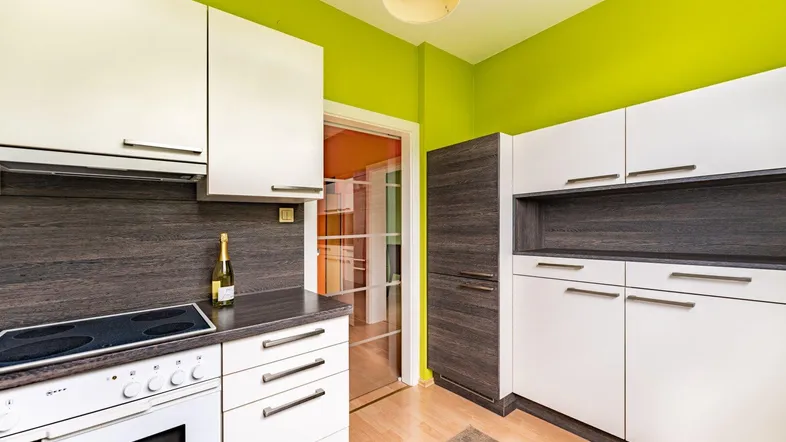 Funktionale Küche mit weißen Schränken, dunkler Arbeitsplatte und leuchtend grünen Wänden.