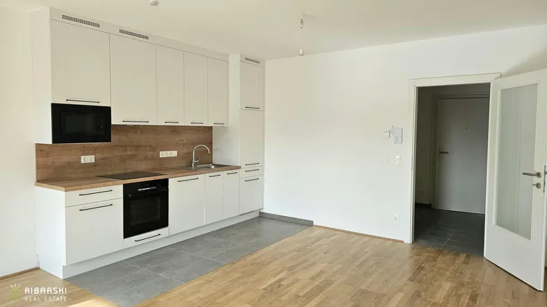 Moderne Einbauküche mit weißen Schränken, Holzarbeitsplatte und integrierten Geräten in offenem Wohnbereich.