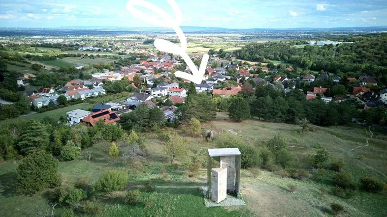Luftaufnahme einer ländlichen Gegend mit Häusern und grünen Hügeln, die auf ein Grundstück zeigt.