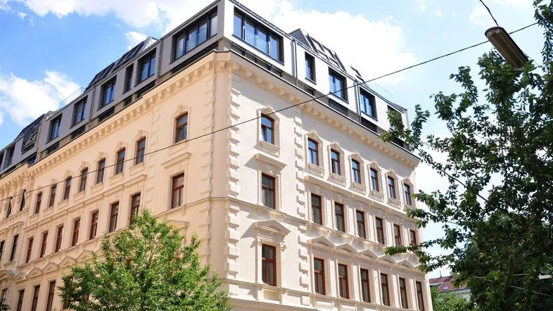 Historisches Gebäude mit modernem Dachausbau und großen Fenstern unter blauem Himmel.