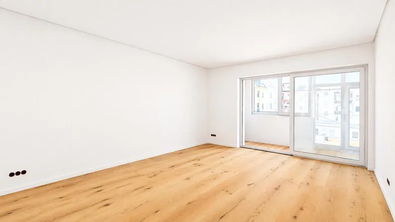 Helles, leeres Zimmer mit neuem Holzboden und Zugang zu einem Balkon.