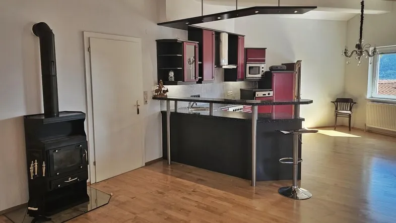 Offener Wohnbereich mit integrierter Küche, Holzofen und Bartheke, ideal für geselliges Beisammensein.