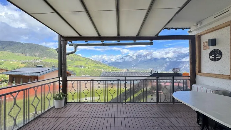 Große überdachte Terrasse mit Holzboden und atemberaubendem Bergblick, ideal zum Entspannen.