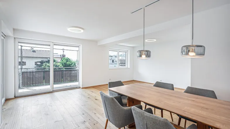 Heller Wohn- und Essbereich mit Holzboden, modernen Pendelleuchten und Zugang zum Balkon.