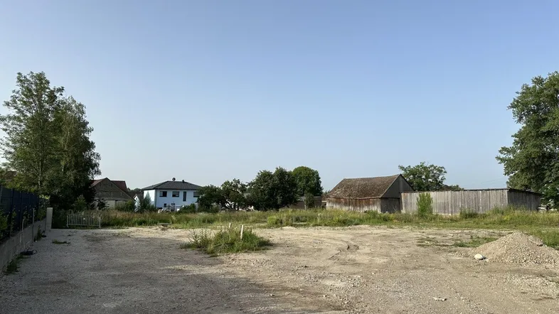 Unbebautes Grundstück in ländlicher Umgebung mit Blick auf benachbarte Häuser und viel Grün.
