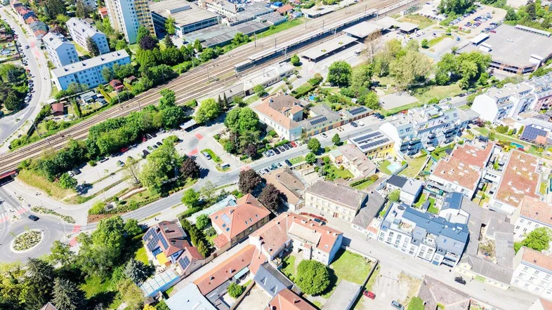 Luftaufnahme einer Stadt mit Wohngebäuden, einer Bahnlinie und viel Grünfläche.