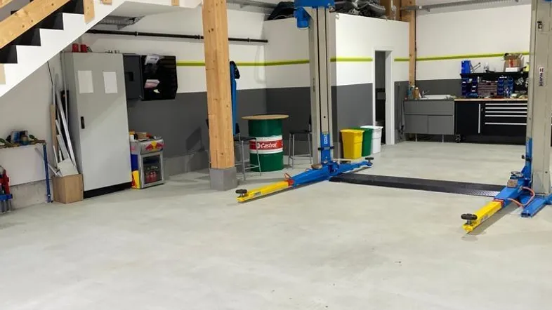 Geräumige Werkstatt mit Holzbalken, Betonboden und einem Fahrzeuglift, bereit für den Betrieb.