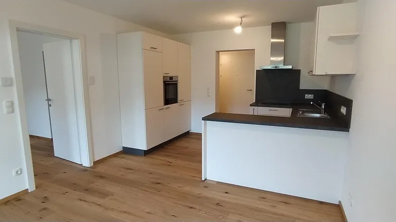 Moderne Küche mit weißen Schränken, dunkler Arbeitsplatte und integriertem Backofen, offen zum Wohnbereich.