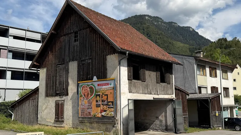 Altes, rustikales Gebäude mit Holzelementen und Ziegeldach, umgeben von Bergen und einem Privatparkplatz.
