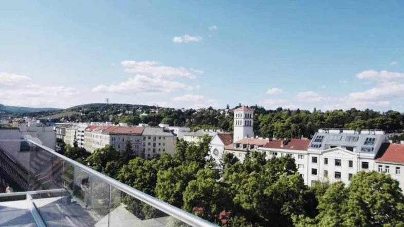Panoramablick über die Stadt mit grünen Hügeln im Hintergrund von einer Dachterrasse.