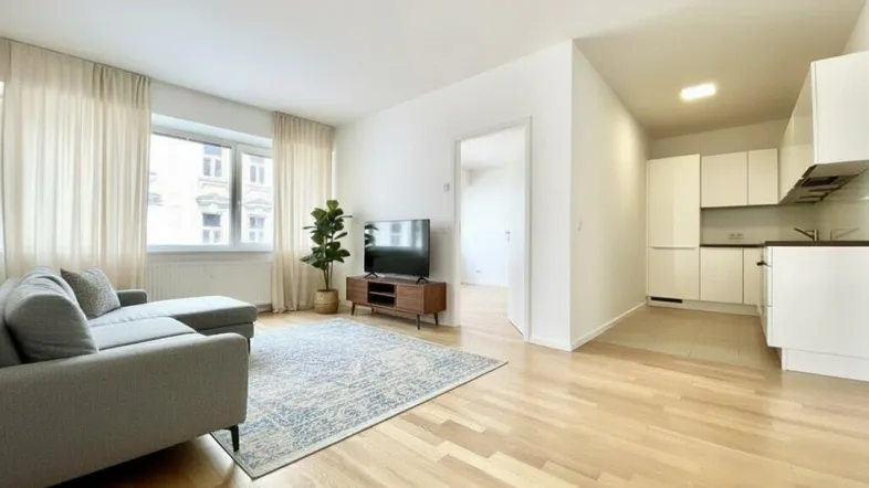 Helles Wohnzimmer mit Parkettboden, Sofa und offener Küchenzeile in modernem Stil.