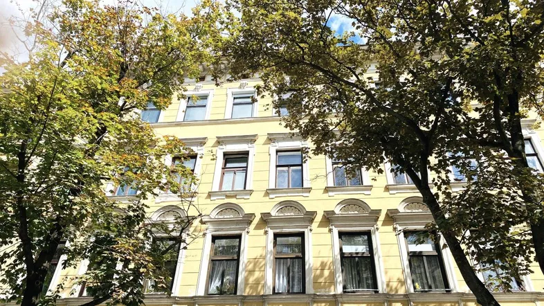 Klassische Fassade eines Mehrfamilienhauses mit vielen Fenstern und Bäumen davor.