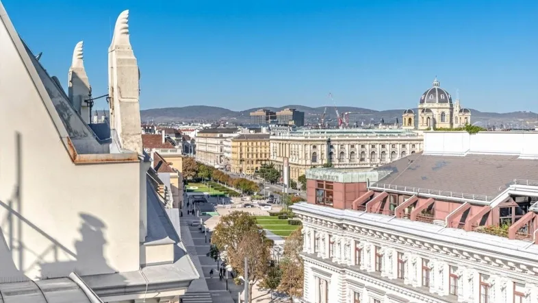 Panoramablick über die Stadt mit historischen Gebäuden und Bergen im Hintergrund unter blauem Himmel.