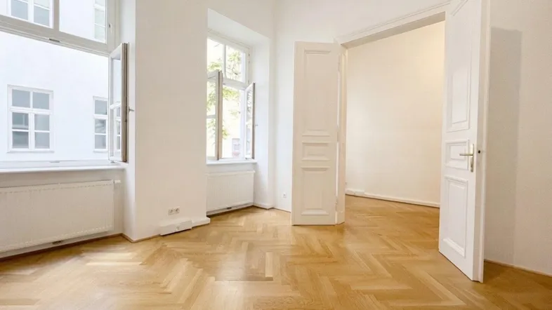 Heller Raum mit Fischgrätparkett, hohen Fenstern und weiß gestrichenen Wänden, bereit zum Einzug.