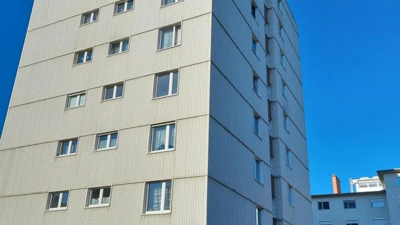 Hohes Mehrfamilienhaus in städtischer Umgebung mit gepflegter Fassade unter blauem Himmel.