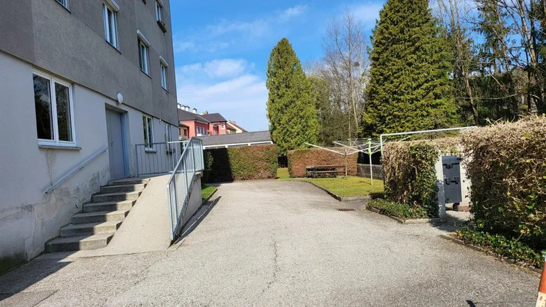 Eingangsbereich eines Mehrfamilienhauses mit Treppe, Rampe und umzäuntem Grünbereich.