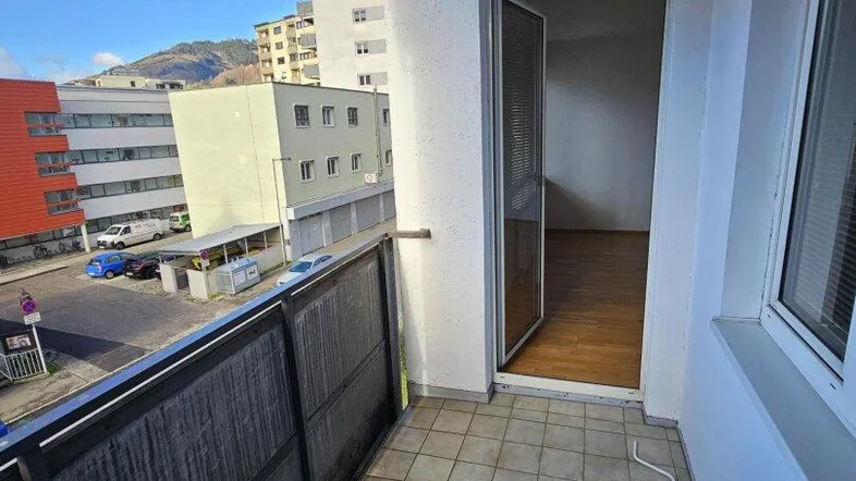 Heller Balkon mit Fliesenboden und Blick auf die umliegenden Gebäude und die Straße.