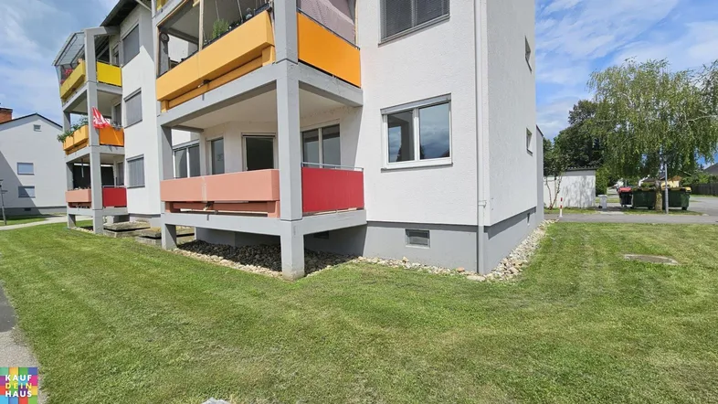 Mehrfamilienhaus mit farbigen Balkonen und gepflegter Rasenfläche im Außenbereich.