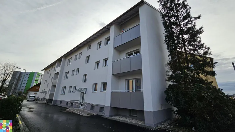 Modernes Mehrfamilienhaus mit Balkonen und barrierefreiem Zugang über eine Rampe.