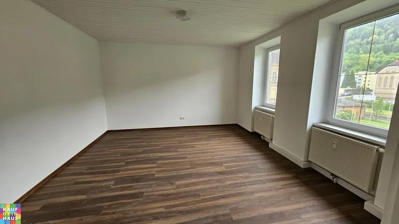 Helles Zimmer mit Laminatboden, weißen Wänden und Blick auf die grüne Umgebung.