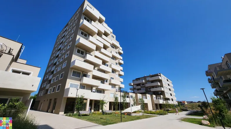 Modernes Wohngebäude mit mehreren Etagen und Balkonen unter blauem Himmel.