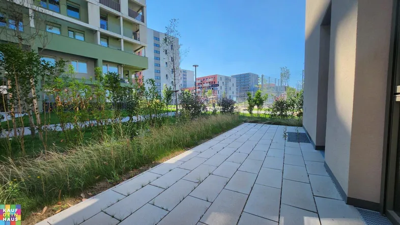 Geräumige gepflasterte Terrasse mit Grünflächen und Blick auf moderne Wohngebäude.