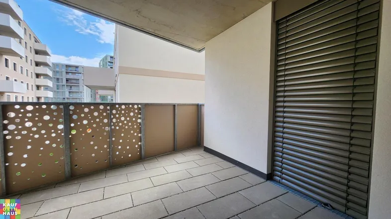 Moderner Balkon mit Fliesenboden, perforiertem Geländer und Blick auf umliegende Gebäude.
