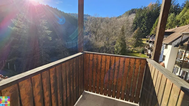 Sonniger Balkon mit Holzboden und weitem Blick über das bewaldete Tal.