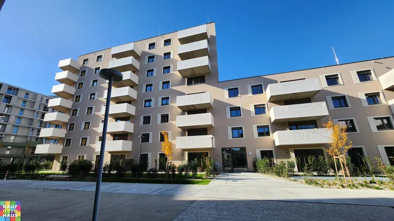 Modernes Mehrfamilienhaus mit zahlreichen Balkonen und klarer Architektur unter blauem Himmel.