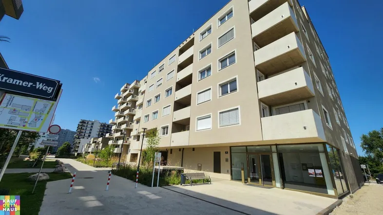 Modernes Mehrfamilienhaus mit klarer Architektur, Balkonen und einer gepflegten Außenanlage unter blauem Himmel.