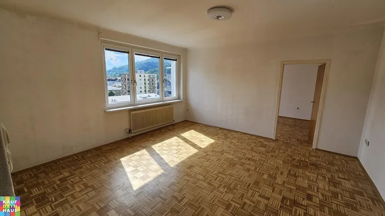 Helles Zimmer mit Parkettboden und großem Fenster, das einen weiten Blick auf die Stadt und Berge bietet.