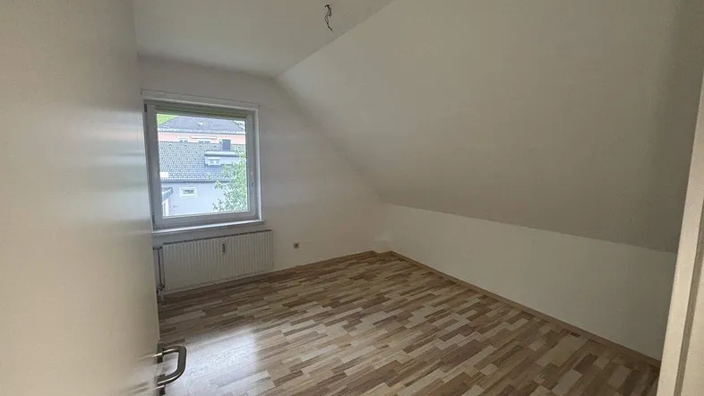 Helles Schlafzimmer mit Dachschräge, Fenster und Laminatboden, bereit zur Einrichtung.
