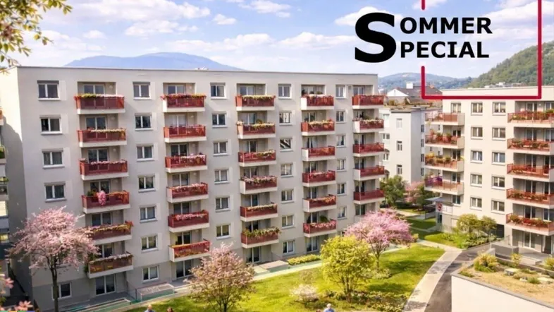 Modernes Mehrfamilienhaus mit roten Balkonen, umgeben von einer gepflegten Grünanlage und Bergblick.